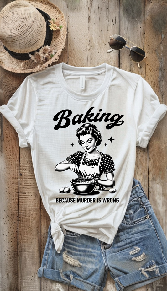 White t-shirt with 'Baking because murder is wrong' graphic on a wooden surface with a hat and sunglasses.